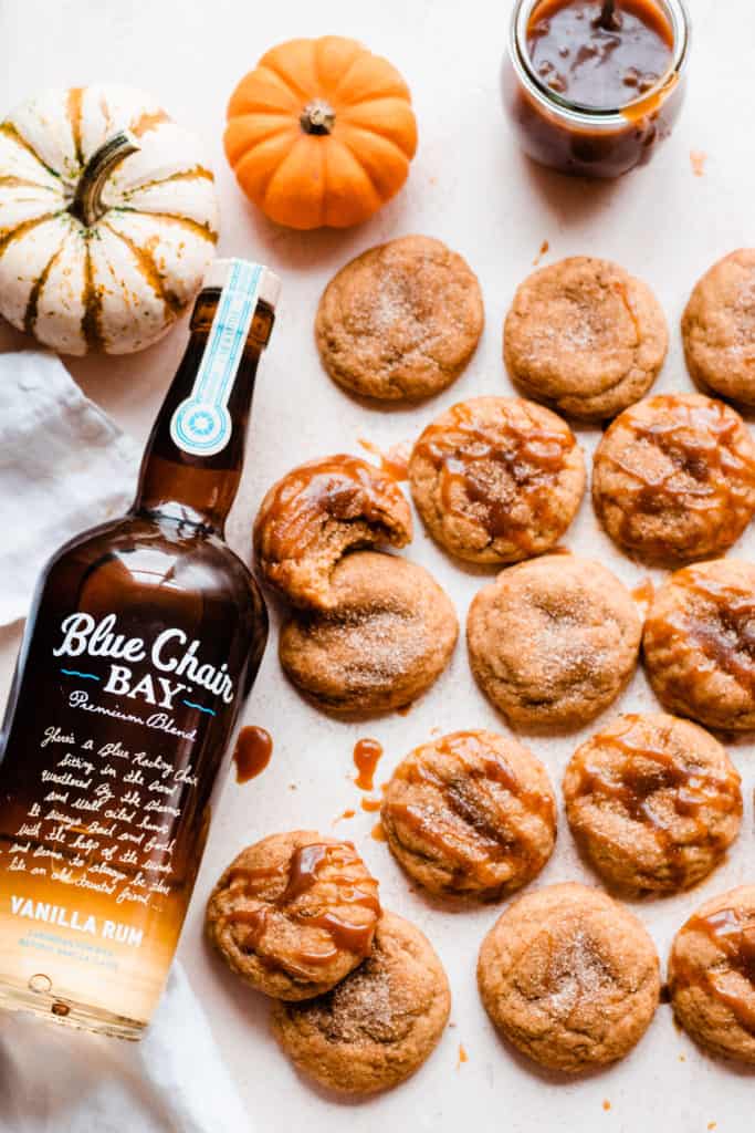 Pumpkin snickerdoodles on a light surface with mini pumpkins, a jar of caramel, and a mug of coffee
