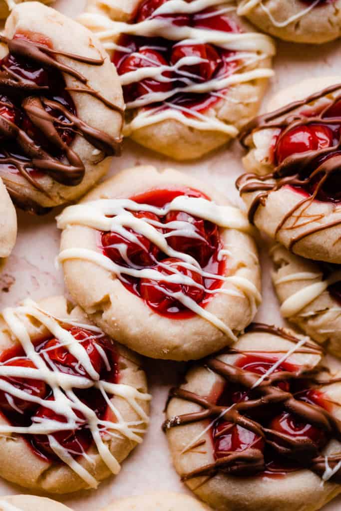 Cherry pie filling filled shortbread cookies drizzled with white and milk chocolate, on a light pink surface