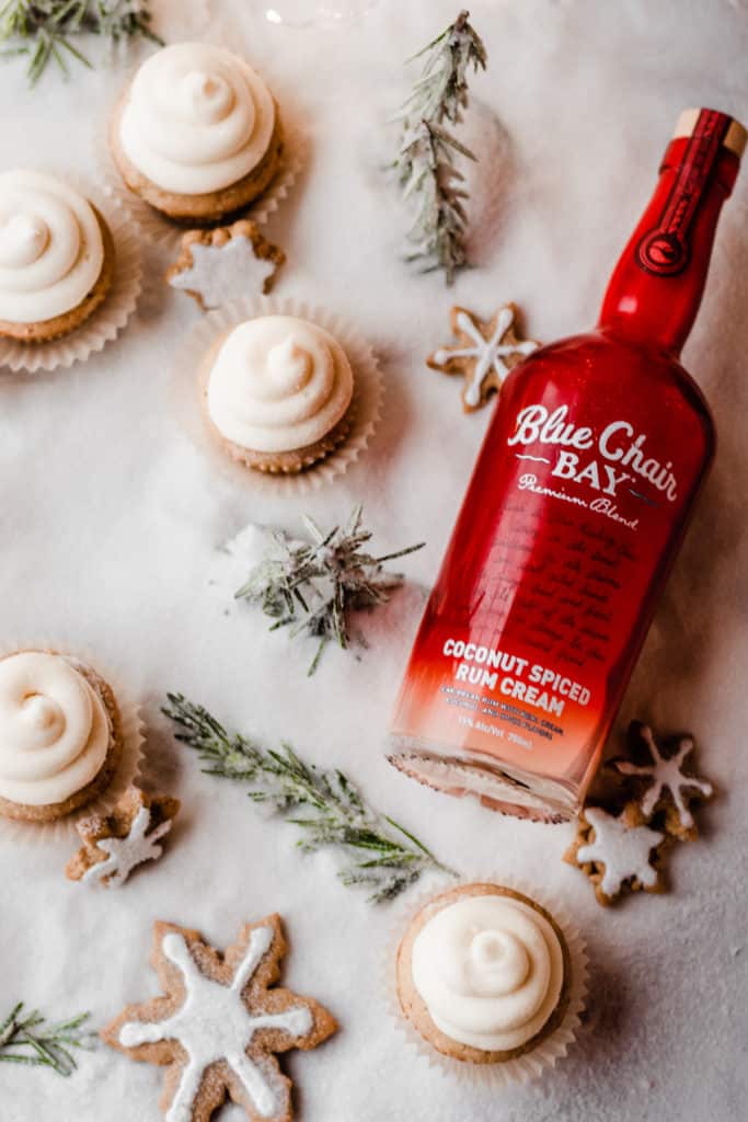 A red bottle of Blue Chair Bay Coconut Spiced Rum Cream in a bed of sugar "snow" with cupcakes and rosemary "trees"