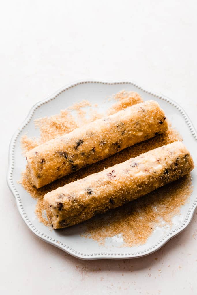 A plate with the two cookie dough logs rolled in raw sugar