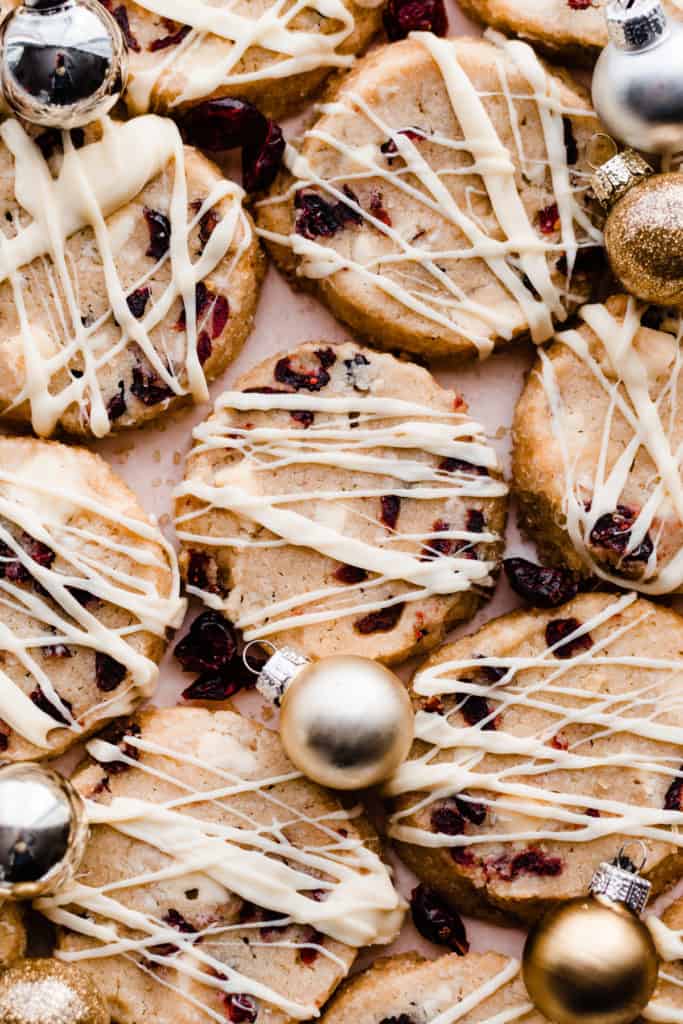 A close-up of a few of the cookies on a light pink surface with mini ornaments and dried cranberries scattered around