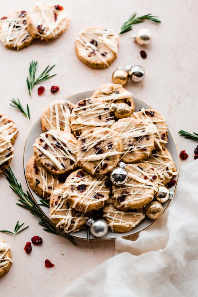 A plate of the cookies with mini ornaments and fresh rosemary scattered around