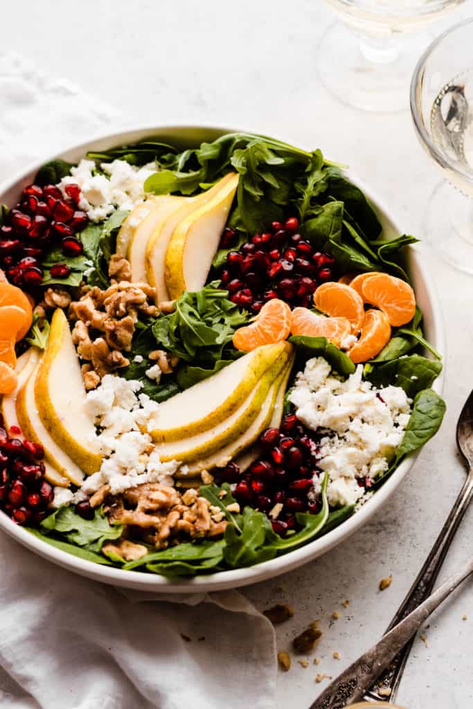 A bowl of greens, pear slices, pomegranates, clementine slices, walnuts, and feta.