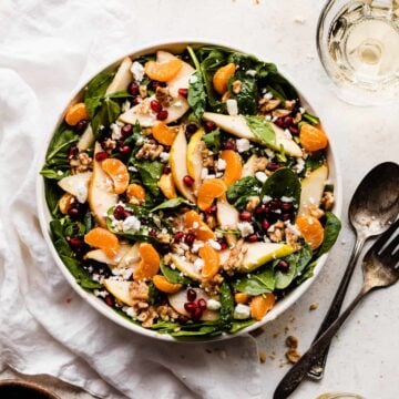 A salad bowl full of fresh greens, sliced pears, pomegranates, mandarin oranges, and walnuts.
