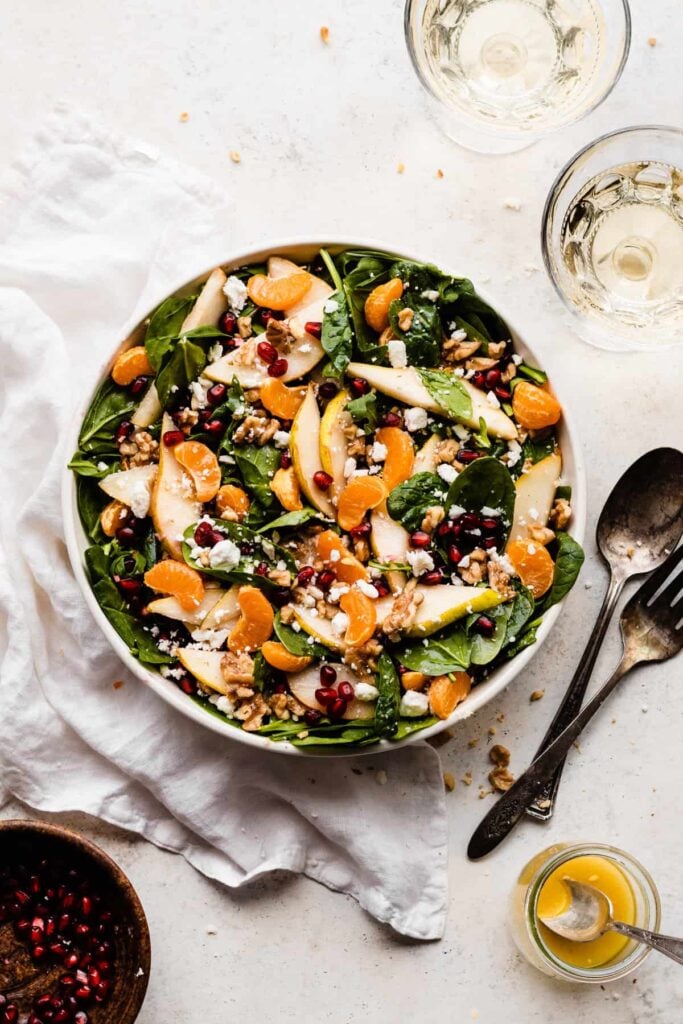 A bowl of tossed salad with pear slices, clementines, pomegranates, walnuts, greens, and feta.
