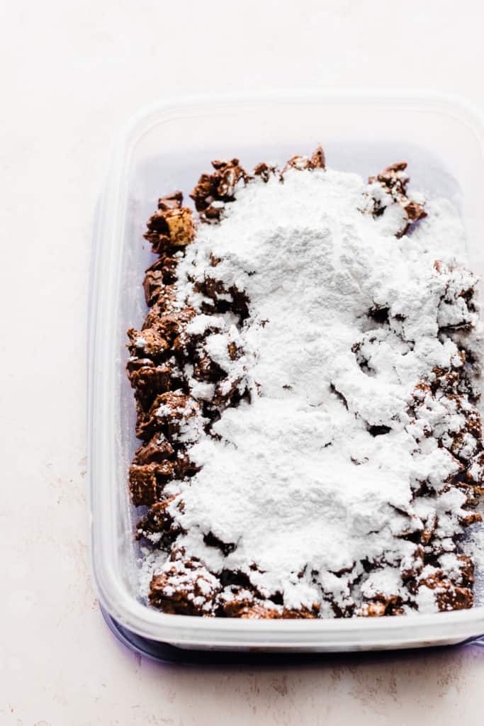 A tupperware container full of the chocolate cereal mixture and powdered sugar