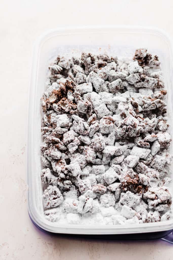 A tupperware filled with powdered sugar coated puppy chow