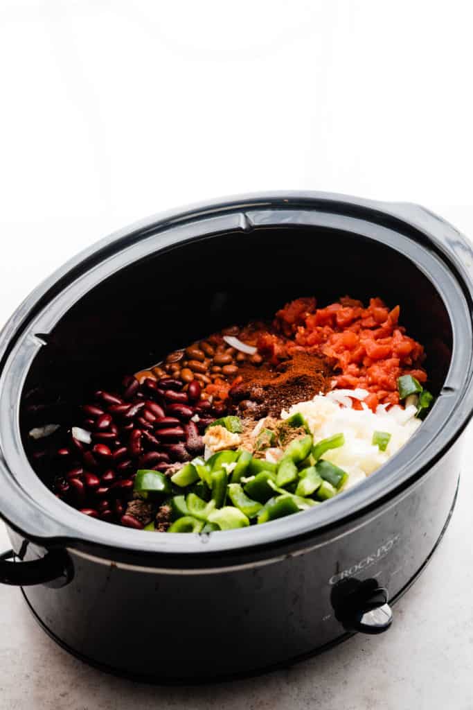 A slow cooker filled with the chili ingredients, before being cooked