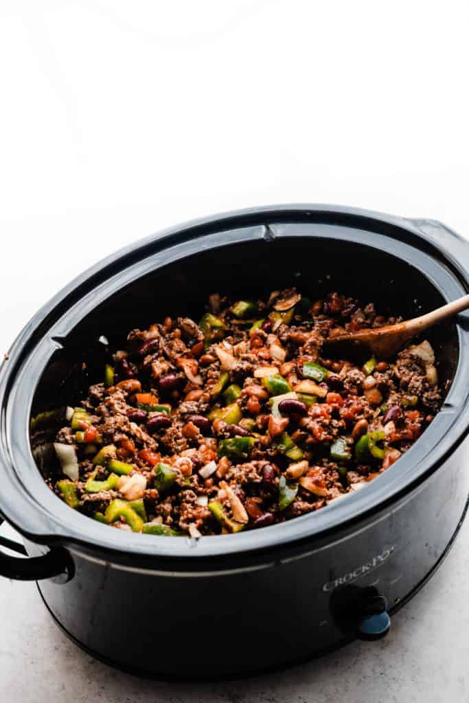 A slow cooker filled with all the chili ingredients, stirred together, before being cooked