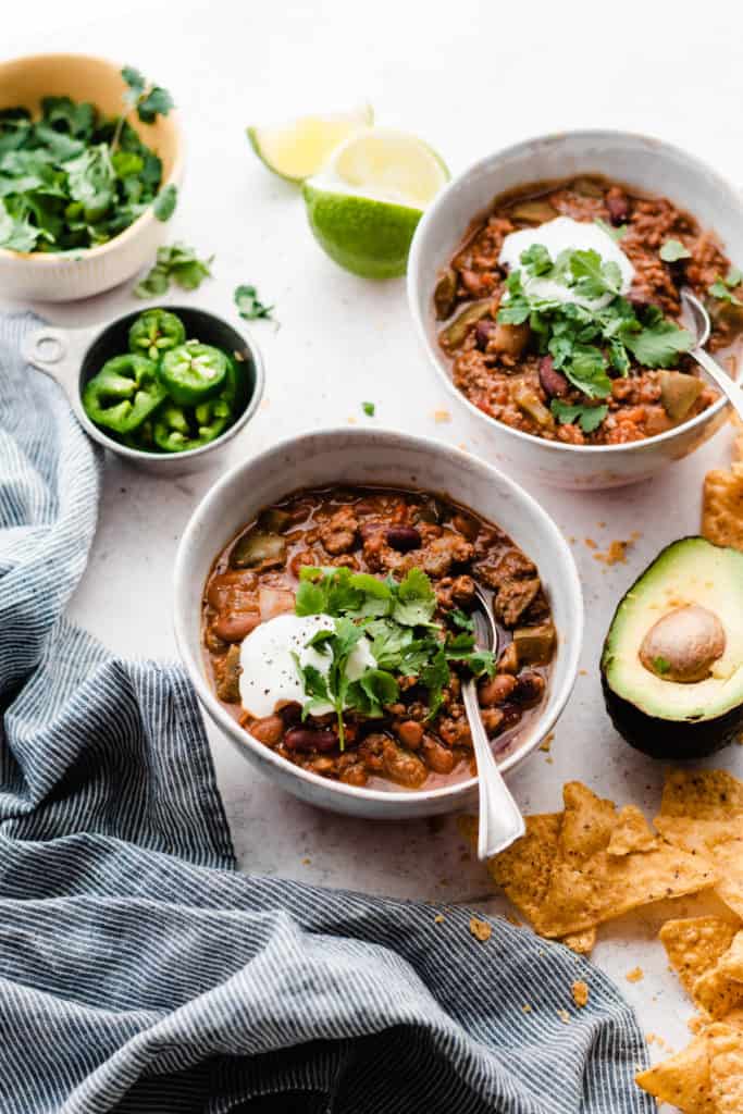 Two bowls of chunky chili topped with sour cream, cilantro, and tortilla chips
