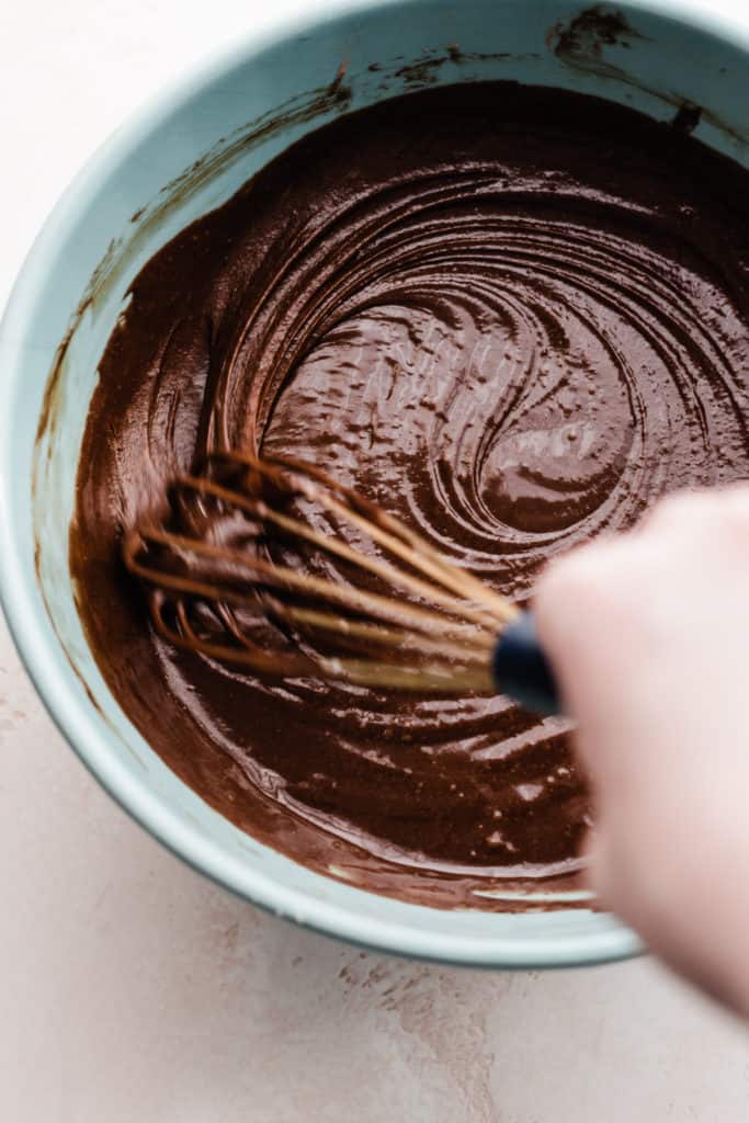A hand whisking chocolate cake batter in a mixing bowl.