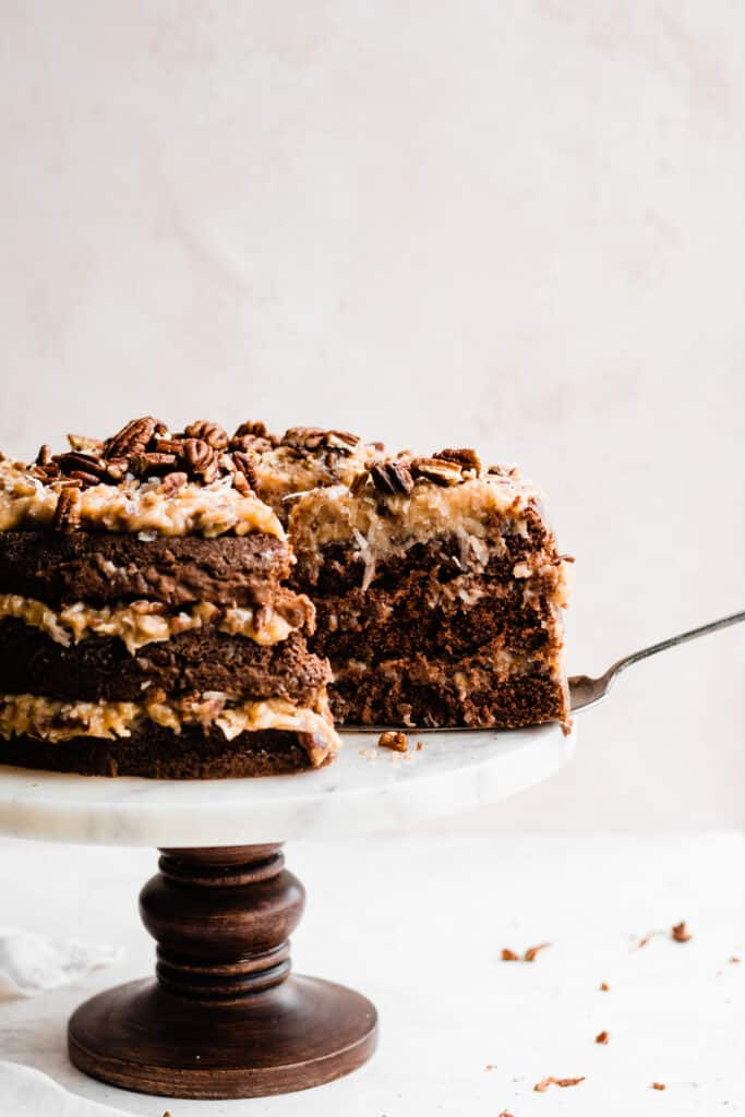 A slice of german chocolate cake being lifted off the cake stand with a server