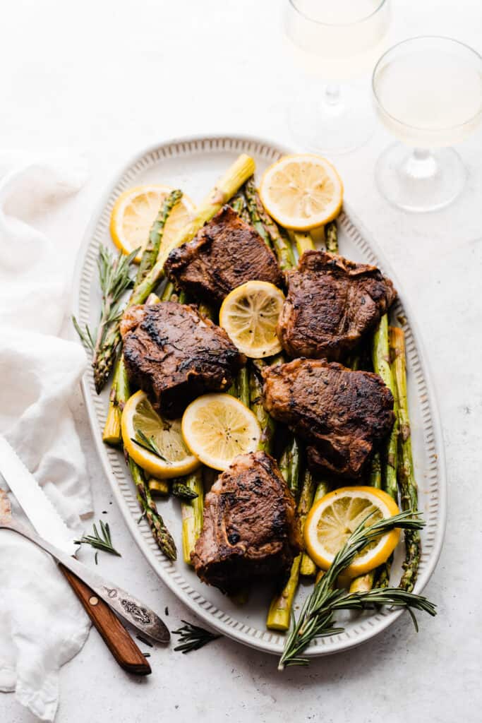 Lamb chops, asparagus, and lemon slices with fresh rosemary on a white platter