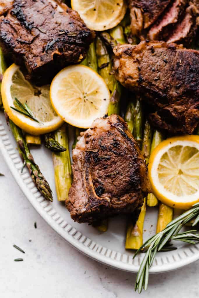 Close up of Lamb chops, asparagus, and lemon slices with fresh rosemary on a white platter