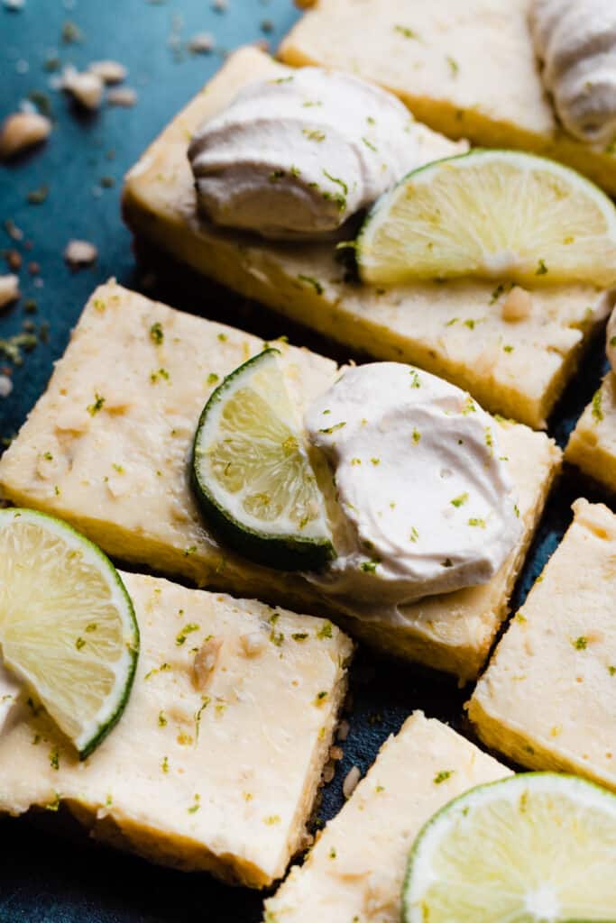 Key Lime Pie bars topped with whipped cream, lime slices and lime zest.