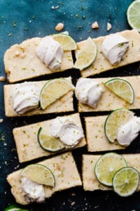 Key Lime Pie Bars on a blue background with dollops of whipped cream & lime slices.