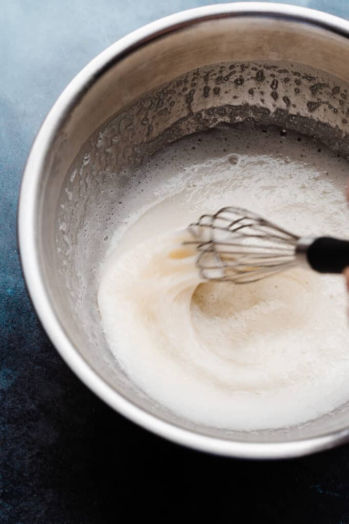 A bowl of the egg white, sugar, and cream of tartar mixture being whisked up.