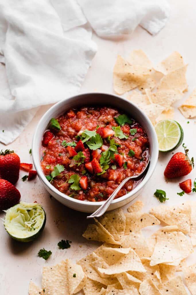 A bowl of strawberry salsa with chips scattered around