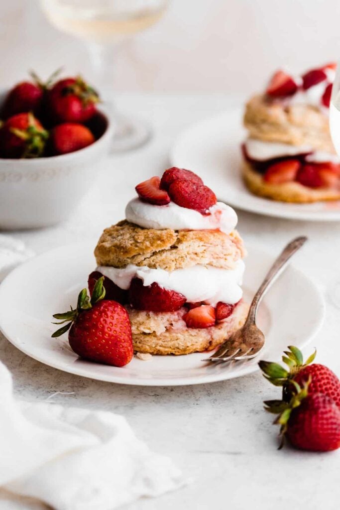Two plates of shortcakes piled high with a cloud of whipped cream and fresh strawberries