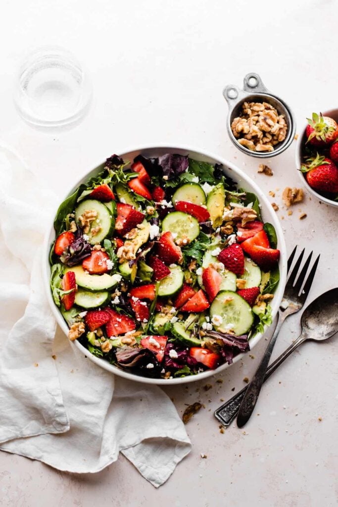 A bowl of strawberry salad with cucumbers, walnuts, feta, and fresh greens.