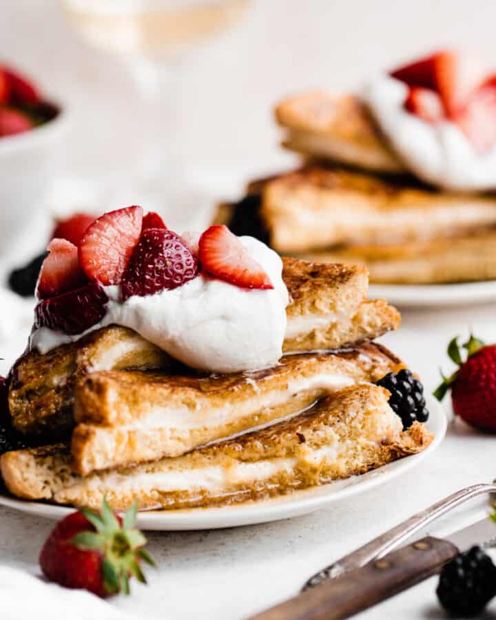 A close-up of a stack of french toast topped with whipped cream, berries, and maple syrup.