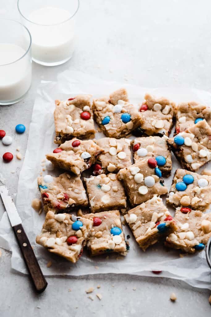 The sliced cookie bars on parchment paper with two glasses of milk nearby. 