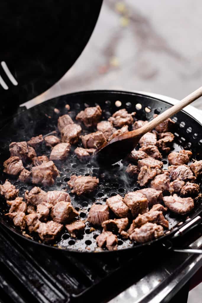 A grill pan with the cubed lamb cooking on the grill. 