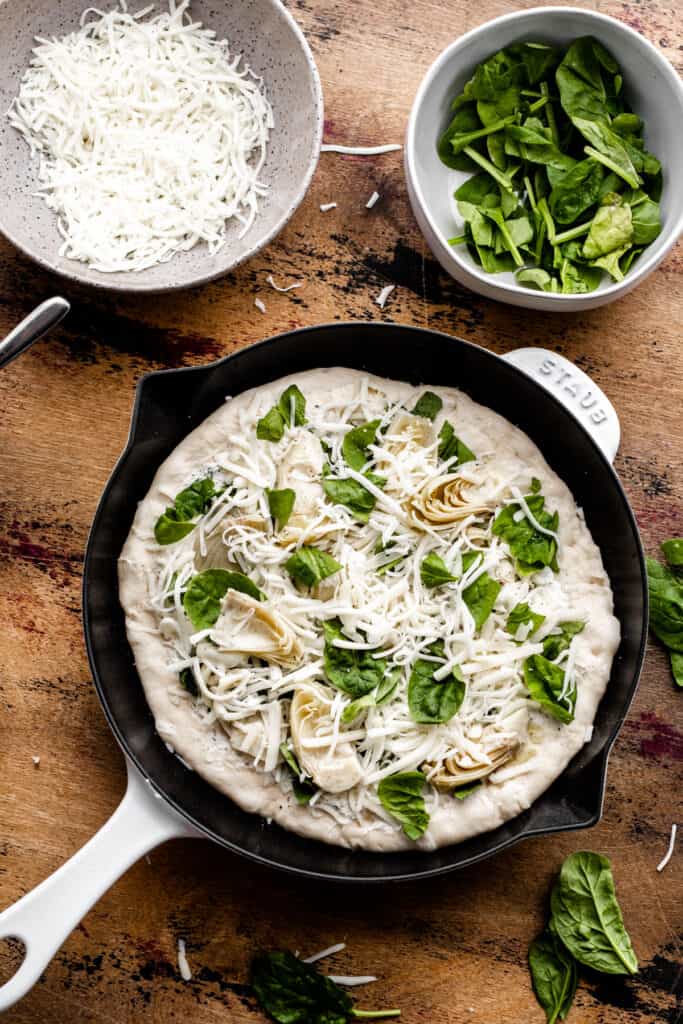 The unbaked, assembled pizza in a cast iron pan on a wood surface. 