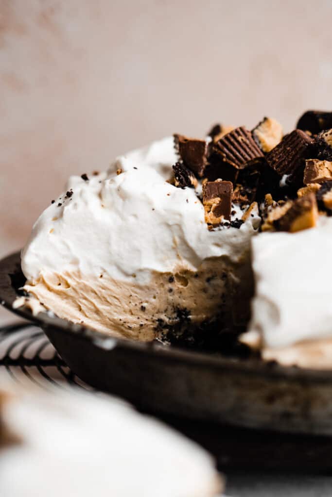 A close-up of a cross-section of the peanut butter pie, with the chocolate crust, peanut butter filling, whipped cream, and peanut butter cups.