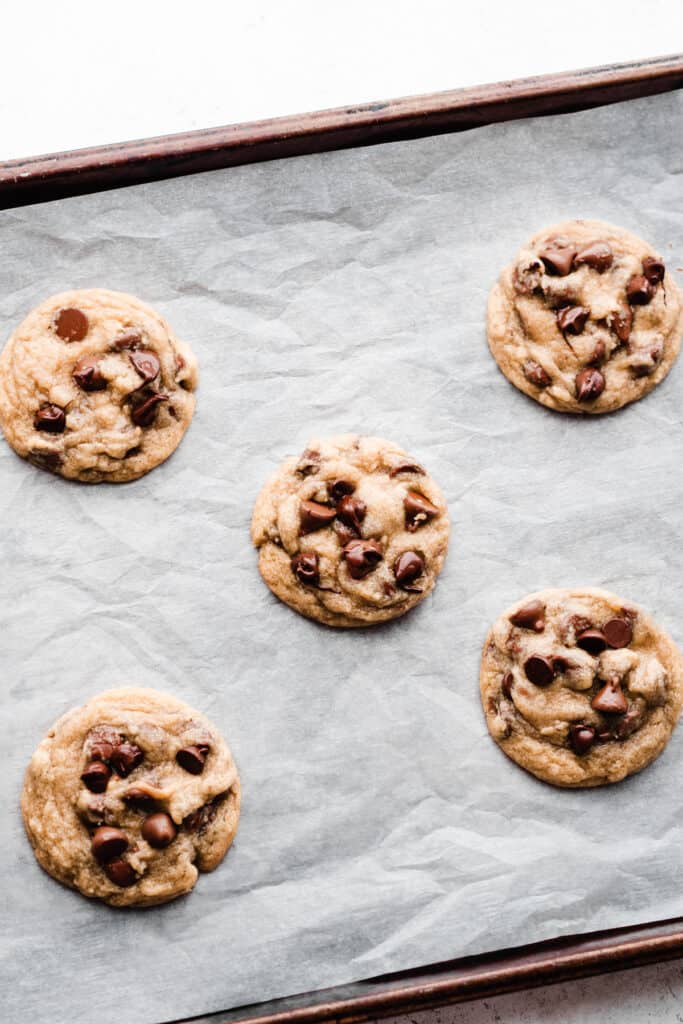 Baked chocolate chip cookies on a parchment paper lined baking sheet.