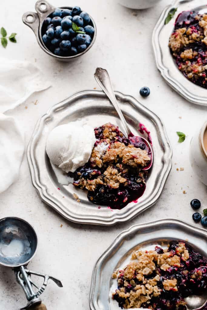 Plates of blueberry crisp topped with vanilla ice cream.