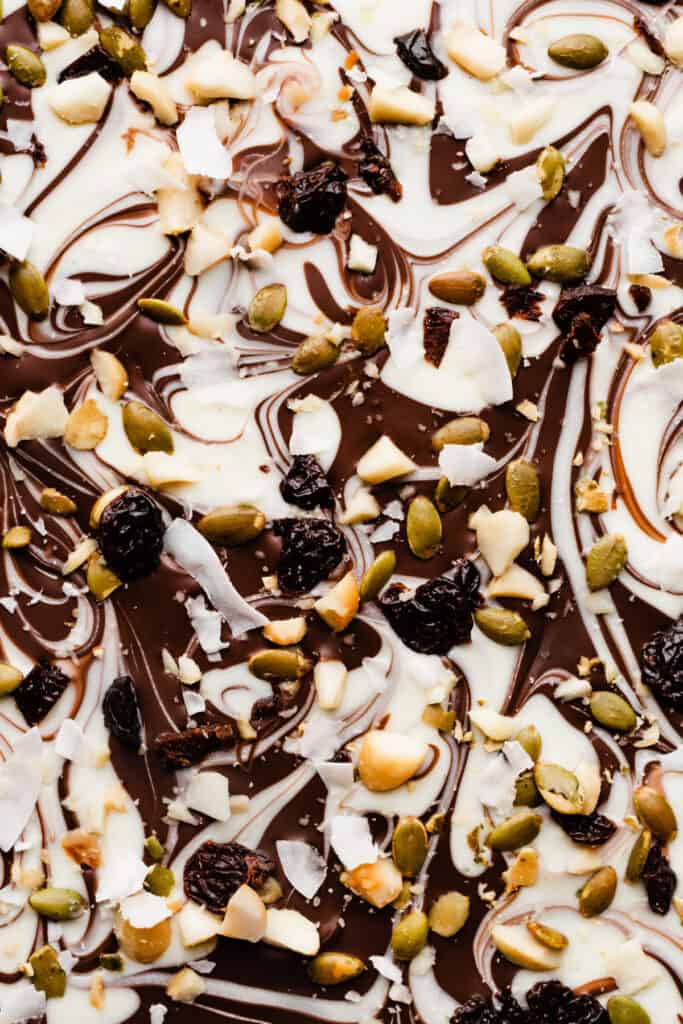 A close-up on the pan of chocolate bark, with the swirls of chocolate topped with dried cherries, pepitas, nuts, and coconut.