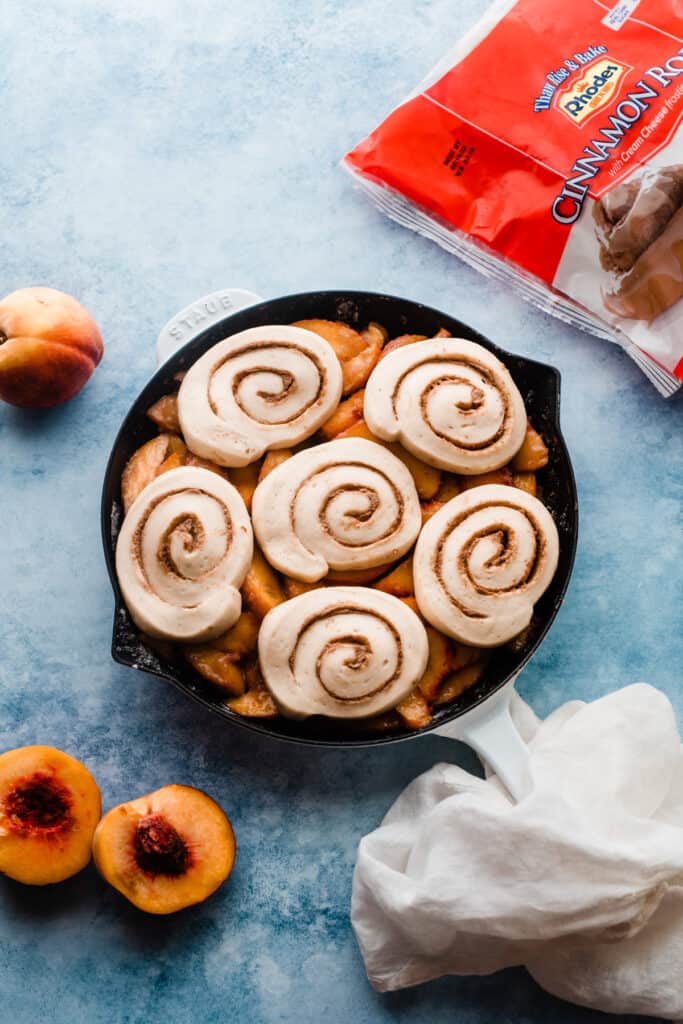 A skillet of peach filling with the unbaked cinnamon rolls on top.