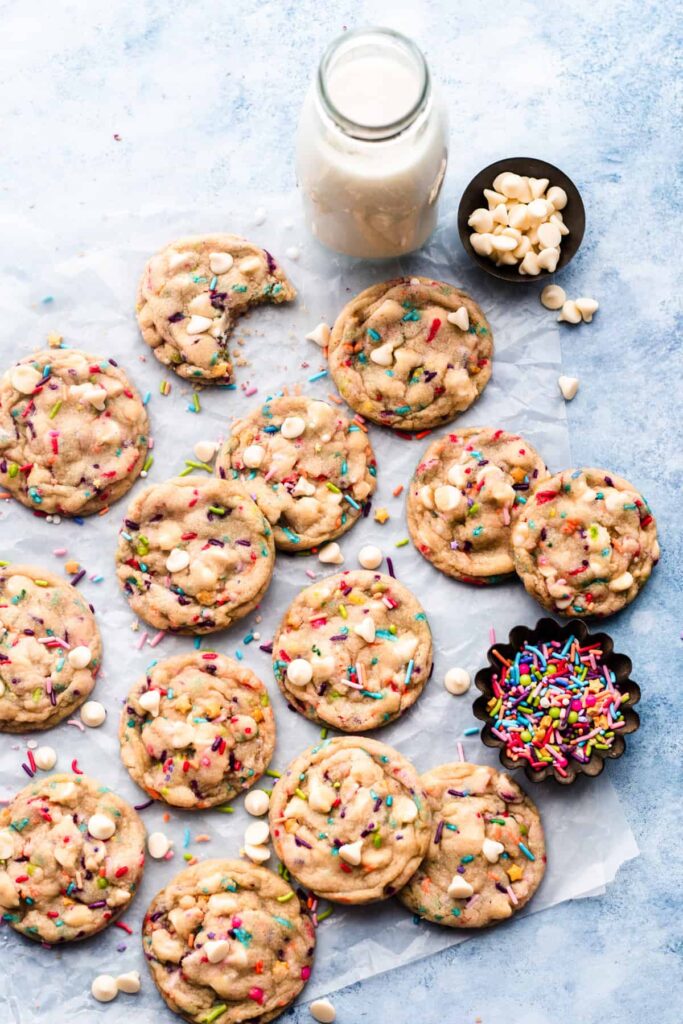 Colorful funfetti cookies on parchment paper with a bottle of milk.