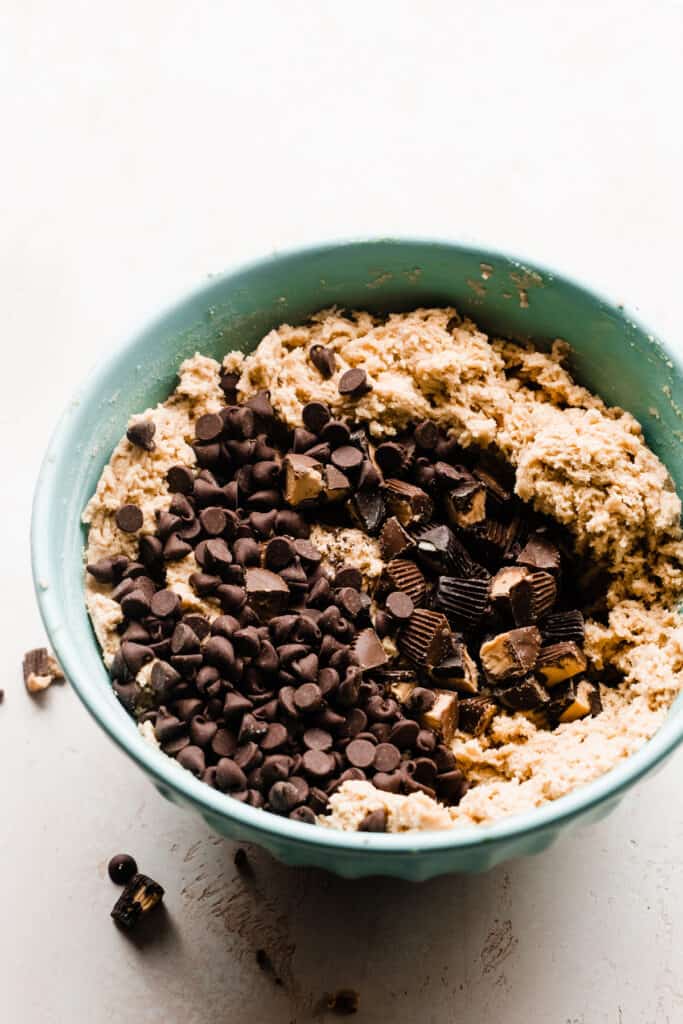 A mixing bowl with peanut butter cookie dough, chocolate chips, and peanut butter cups. 