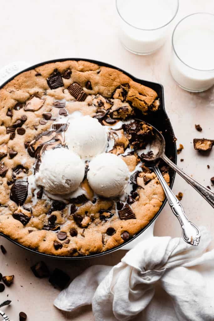 A skillet cookie with scoops of ice cream on top, and spoons digging in.