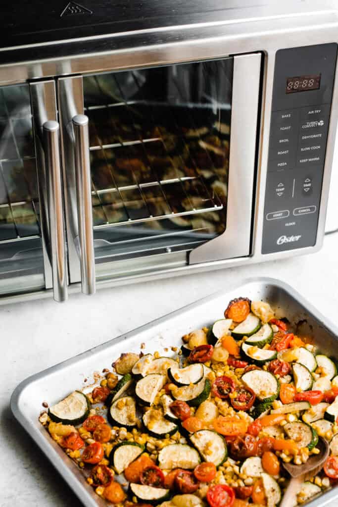 A pan of the roasted veggies sitting next to a french door air fryer.