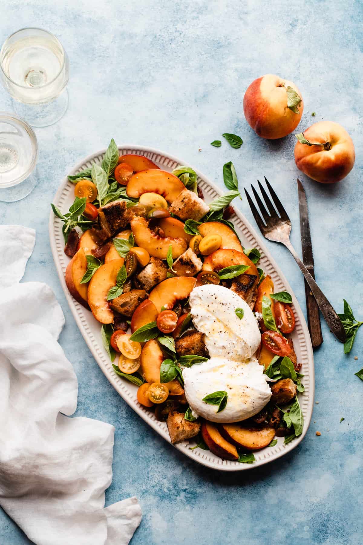 A peach salad with burrata, tomatoes, bacon, and basil on a platter.