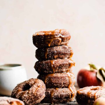 A stack of apple cider donuts coated in apple pie spice sugar and dripping in caramel sauce.