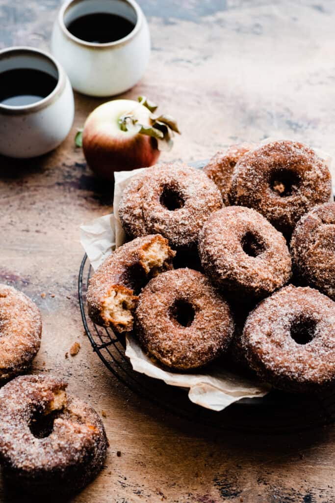 Apple cider donuts in a pan, with cups of coffee nearby 