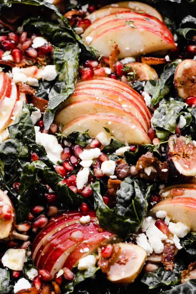 A close-up of the sliced apples, feta, and pomegranate arils laying in a bed of kale.