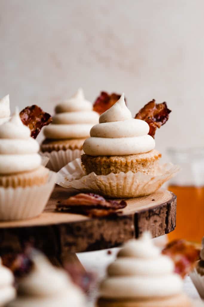 A close-up of the maple bacon cupcakes on a wooden cake stand.