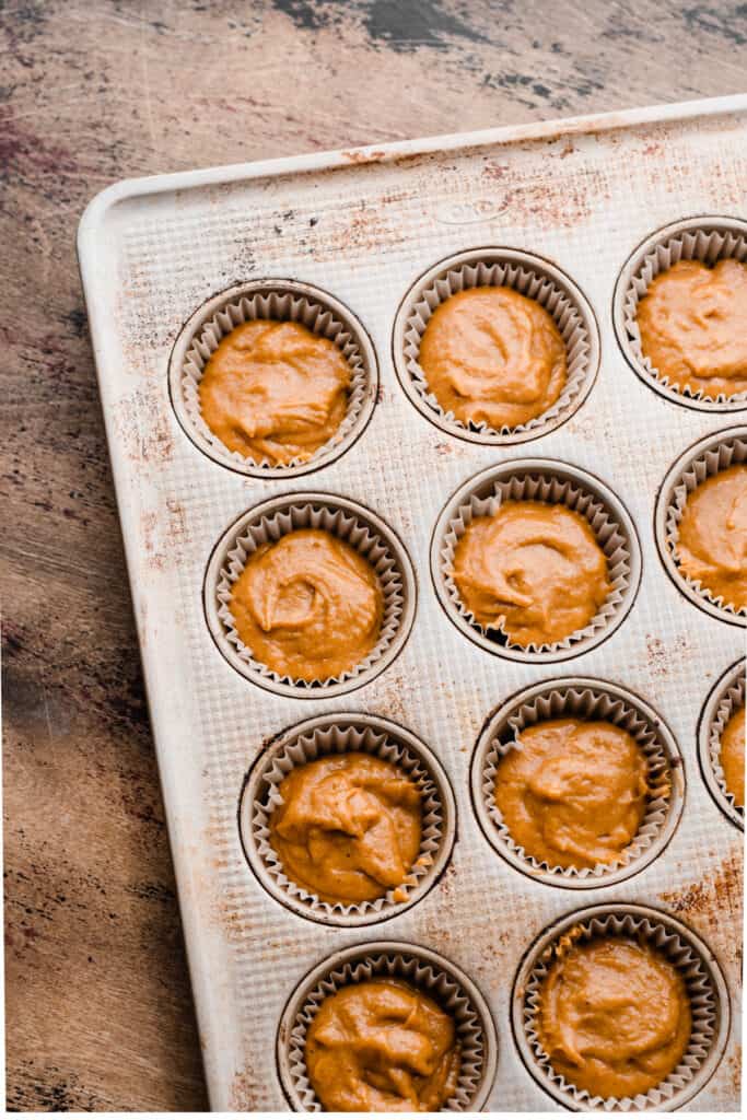 A muffin pan with paper liners filled with pumpkin muffin batter.
