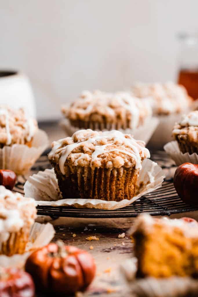 A close-up of a pumpkin muffin drizzled with maple glaze, on a cooling rack.