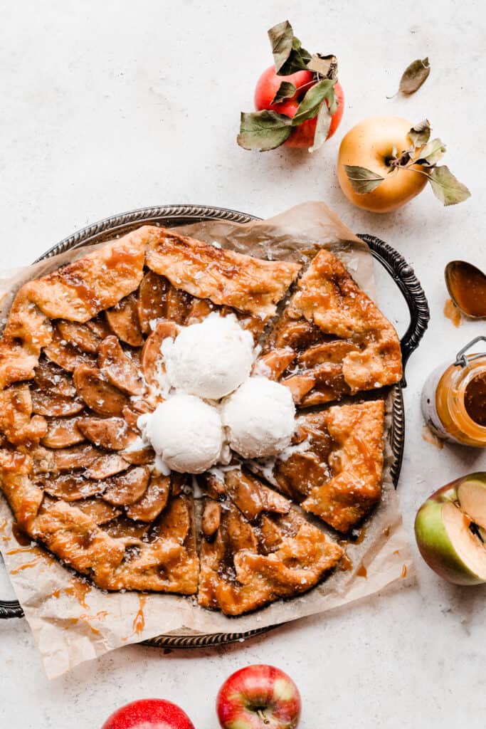 A caramel apple galette on a metal tray topped with vanilla ice cream.