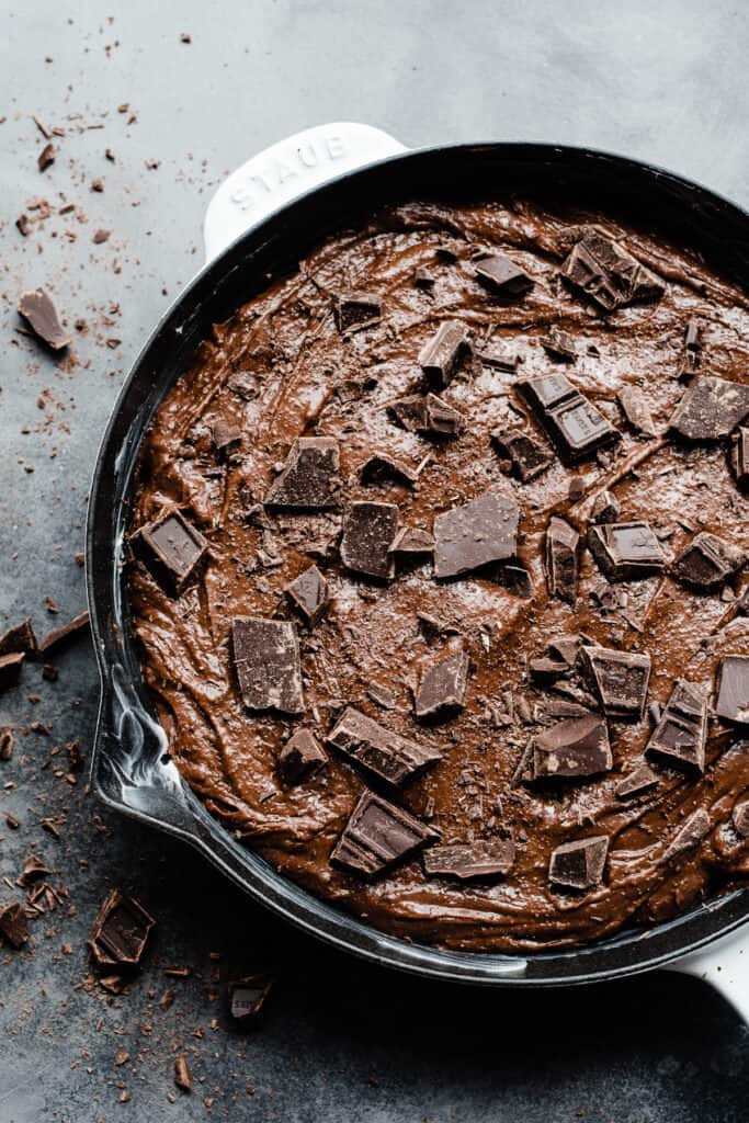 A skillet filled with brownie batter and topped with chocolate chunks.