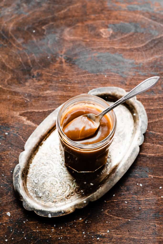 A jar of salted caramel sauce on a wooden surface.