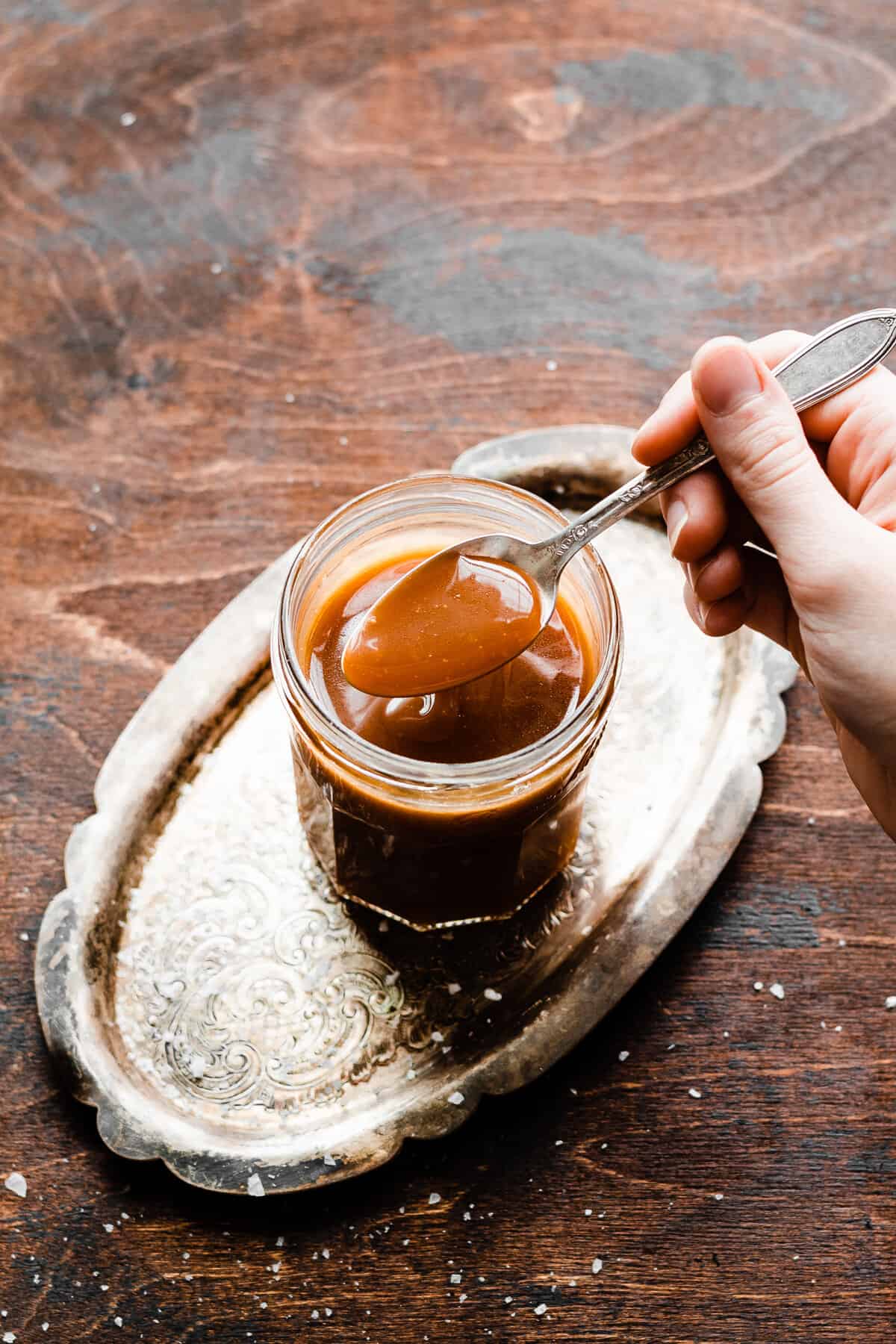 A spoon dipping into a jar of caramel sauce.