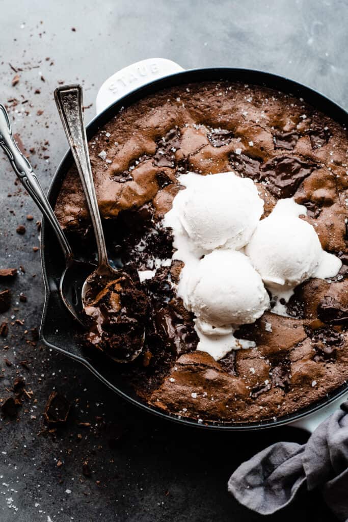 A skillet brownie with a few bites missing, topped with vanilla ice cream.