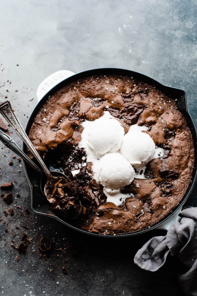A skillet brownie topped with ice cream and with two spoons digging in.